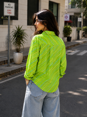 A woman wearing a bright lime green long-sleeve button-up shirt with diagonal yellow and blue stripes, paired with light-wash wide-leg jeans, standing on a city street.